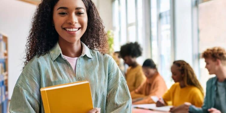 Estudante sorrindo com livros, representando o aumento da bolsa-estágio para 14 mil alunos.
