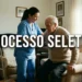 Cuidadora auxiliando idoso a levantar do sofá ilustrando o processo seletivo para vaga de cuidador.