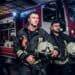Bombeiros em frente a um caminhão de bombeiros, prontos para uma emergência, durante a noite, com equipamentos de proteção.