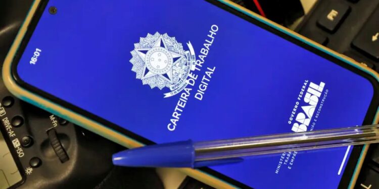 Celular com aplicativo da Carteira de Trabalho Digital aberto sobre mesa com teclado e caneta.