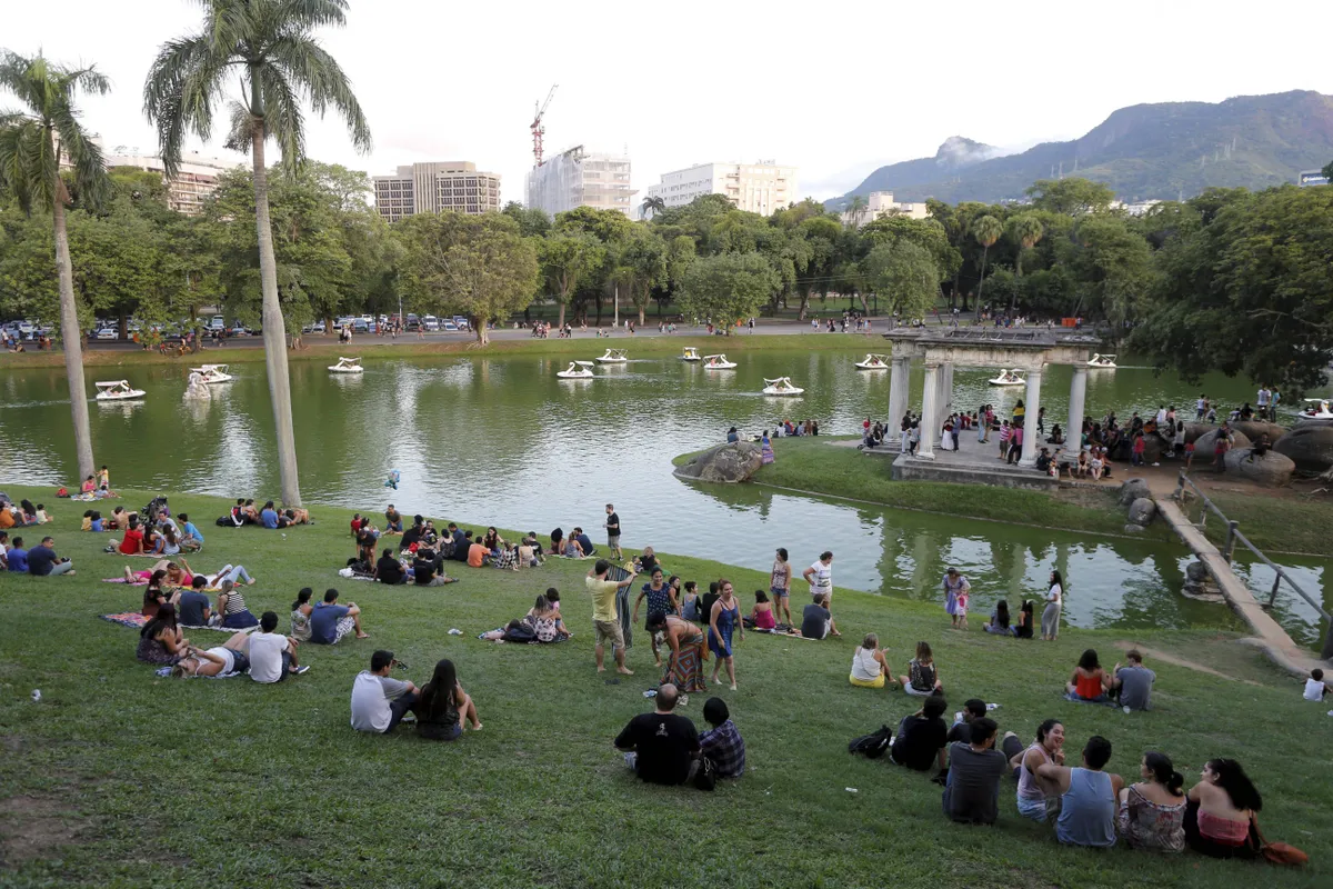 Quinta da Boa Vista com visitantes sentados no gramado, lago com pedalinhos e área arborizada ao fundo.