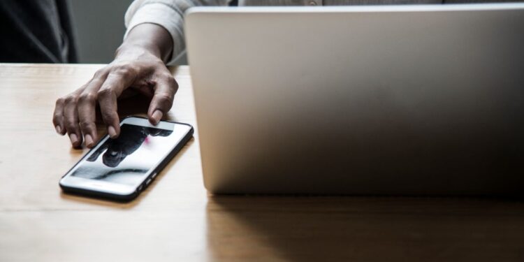 Pessoa trabalhando em um laptop com um smartphone ao lado, representando as mudanças nas regras de acesso aos serviços digitais da Receita Federal, incluindo autenticação via conta gov.br e representação digital.