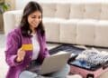 Mulher sorrindo enquanto planeja sua viagem usando um laptop e segurando um cartão de crédito, destacando a facilidade da busca por passagens aéreas com ferramentas como o Skyscanner integrado ao ChatGPT.