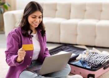 Mulher sorrindo enquanto planeja sua viagem usando um laptop e segurando um cartão de crédito, destacando a facilidade da busca por passagens aéreas com ferramentas como o Skyscanner integrado ao ChatGPT.