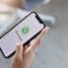 Pessoa segurando smartphone com tela inicial do WhatsApp exibida, ilustrando mudanças de personalização no aplicativo.