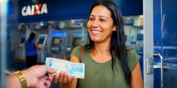 Mulher recebendo dinheiro em frente à Caixa, em referência ao pagamento do Abono Salarial para os nascidos em novembro e dezembro.