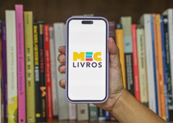 MEC Livros biblioteca digital gratuita - mão segurando smartphone com logo MEC Livros em frente a estante de livros