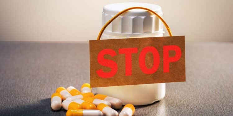 Medicamentos e cápsulas com placa de “stop”, representando proibição de produtos irregulares pela Anvisa.