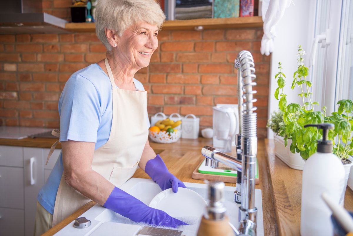 Dona do lar lavando louça na cozinha e buscando informações sobre aposentadoria, contribuição facultativa ao INSS e BPC LOAS.