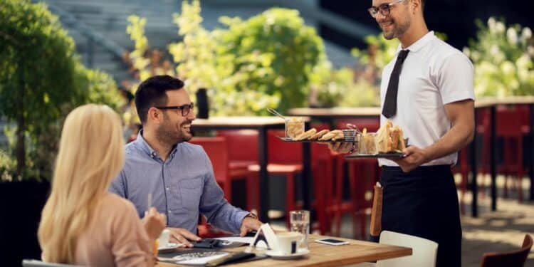 Garçom servindo bebidas e petiscos a clientes em um restaurante ao ar livre. Profissional de atendimento trabalhando com escalas 6x1.