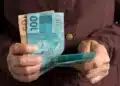 Pessoa segurando notas de 100 e 50 reais, ilustrando o auxílio do INSS sem necessidade de consulta médica.