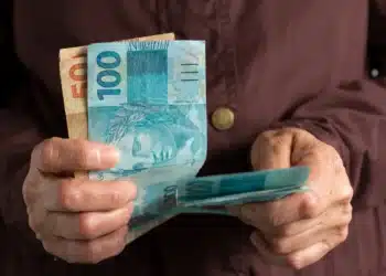 Pessoa segurando notas de 100 e 50 reais, ilustrando o auxílio do INSS sem necessidade de consulta médica.