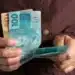Pessoa segurando notas de 100 e 50 reais, ilustrando o auxílio do INSS sem necessidade de consulta médica.