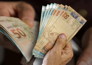 Pessoa segurando cédulas de real representando pagamentos de benefícios sociais em maio.