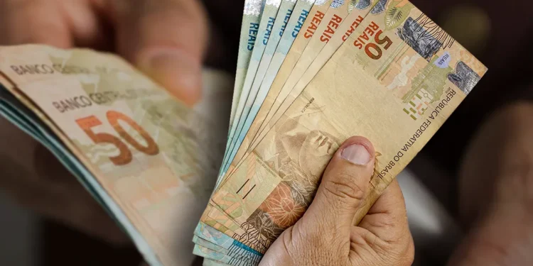 Pessoa segurando cédulas de real representando pagamentos de benefícios sociais em maio.