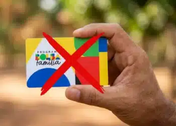 Mão segurando cartão do Bolsa Família com X vermelho, sinalizando cortes.
