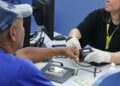 Atendente com luvas brancas realizando coleta de impressão digital de cidadão em posto de atendimento do governo
