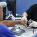 Atendente com luvas brancas realizando coleta de impressão digital de cidadão em posto de atendimento do governo