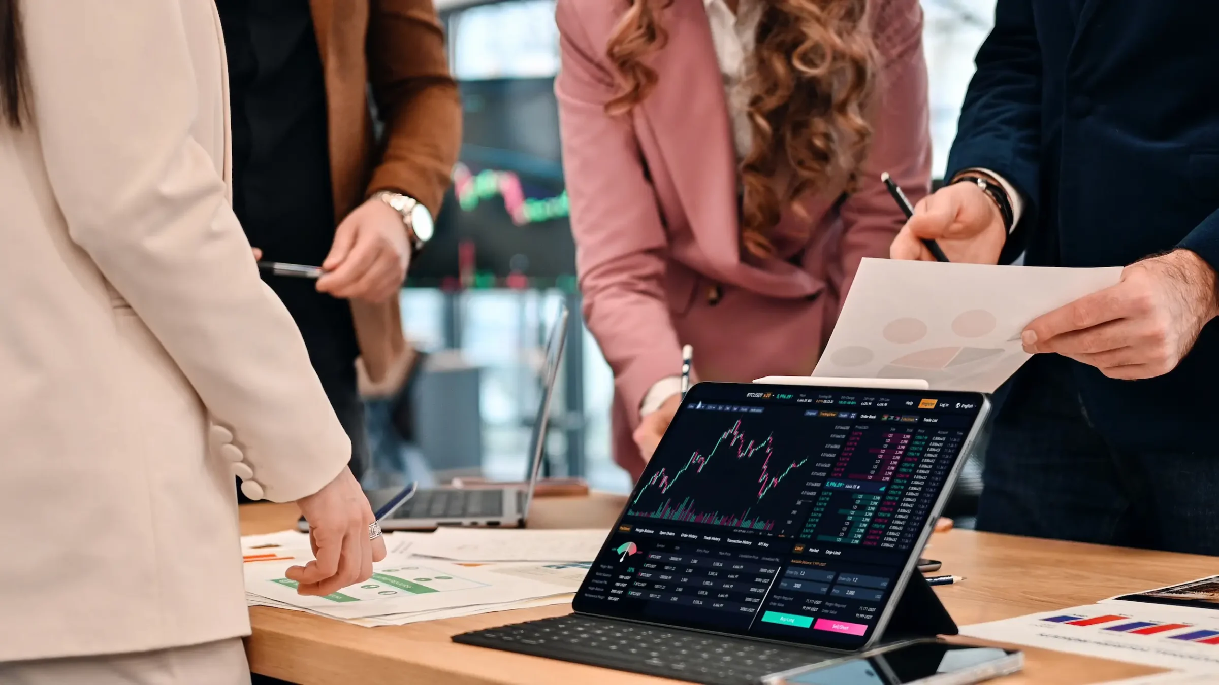 Equipe analisando gráficos financeiros em tablet e documentos durante planejamento de carreiras no mercado financeiro.