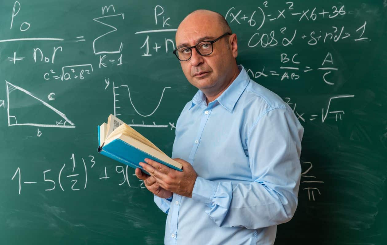Professor em frente ao quadro com fórmulas matemáticas, representando carreira com alta remuneração e menor nível de estresse.