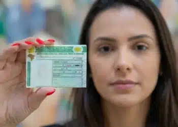 Mulher segurando sua carteira de motorista brasileira, destacando o documento em primeiro plano.
