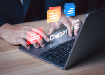 Pessoa digitando em laptop cinza com balões de conversa coloridos e texto "ChatGPT" na tela