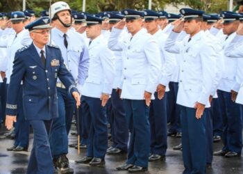 Militar da Aeronáutica com fardamento azul e medalhas passa em revista tropa de cadetes uniformizados prestando continência