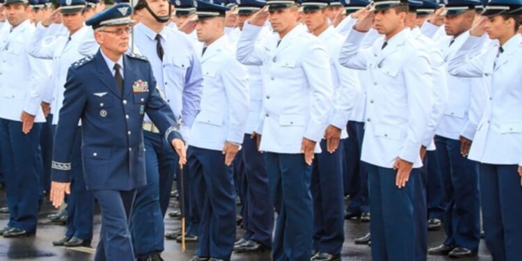Militar da Aeronáutica com fardamento azul e medalhas passa em revista tropa de cadetes uniformizados prestando continência