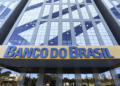 Edifício corporativo com fachada de vidro azul e amarelo com letreiro Banco do Brasil na entrada