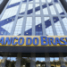 Edifício corporativo com fachada de vidro azul e amarelo com letreiro Banco do Brasil na entrada