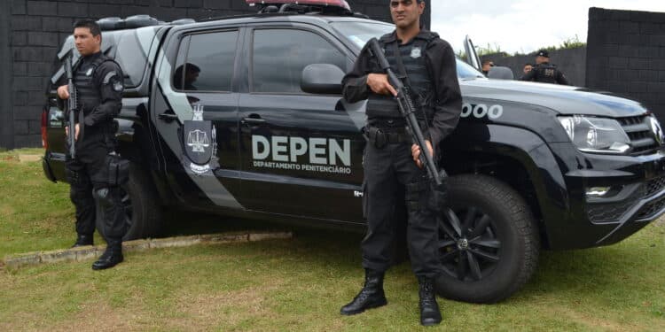 Dois policiais penais fardados e armados posam ao lado de viatura oficial do DEPEN Paraná