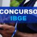 Mãos de agente do IBGE segurando caneta azul, com crachá e cordão institucional do instituto