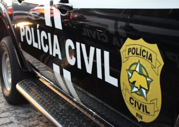 Viatura preta da Polícia Civil com brasão dourado sobre anúncio do concurso da PC do Acre com 139 vagas