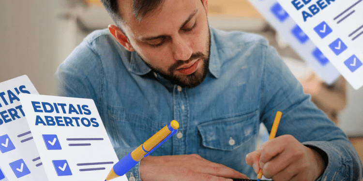 Homem barbudo de camisa jeans escreve em caderno com caneta amarela, cercado por checklists de editais abertos
