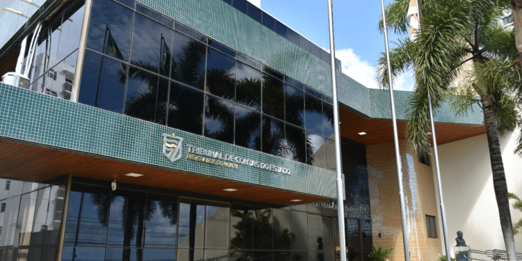 Fachada do Tribunal de Contas do RN com revestimento verde e faixas douradas, palmeiras e bandeiras