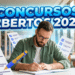 Homem barbudo de óculos e camisa verde estuda em biblioteca, escrevendo em caderno com checklists ao redor