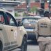 Dois policiais da PM da Bahia de costas, fardados em bege, ao lado de viatura com inscrição 8ª CIPM