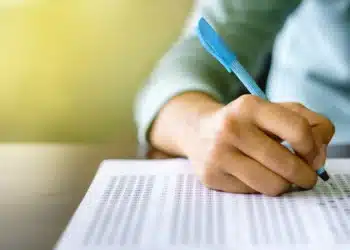 Pessoa preenchendo uma folha de respostas de concurso, simbolizando os processos seletivos para vagas no setor público, com foco nas vítimas de violência doméstica na Paraíba.