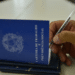 Cargos CLT maiores salários - mão segurando caneta sobre Carteira de Trabalho e Previdência Social azul