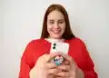 Mulher sorrindo e usando um smartphone com pop socket, criando figurinhas no WhatsApp.