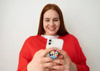 Mulher sorrindo e usando um smartphone com pop socket, criando figurinhas no WhatsApp.