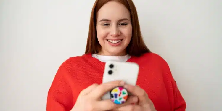 Mulher sorrindo e usando um smartphone com pop socket, criando figurinhas no WhatsApp.