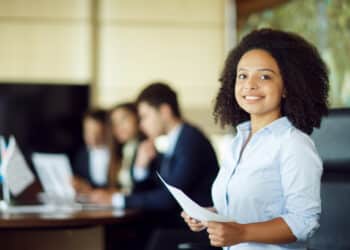 Jovem profissional sorrindo com documentos nas mãos em ambiente corporativo sobre cursos gratuitos da Petrobras com 1.540 vagas