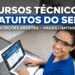Estudante sorridente usando óculos de proteção e uniforme azul opera notebook em laboratório do SENAI