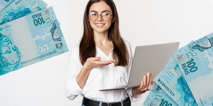 Jovem segurando notebook com notas de cem reais ao redor representando auxílio mensal de R$ 800 para cursos.