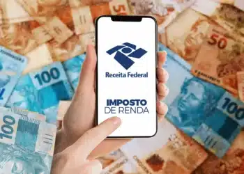 Mão segurando smartphone com logo da Receita Federal e texto "Imposto de Renda" sobre notas de real