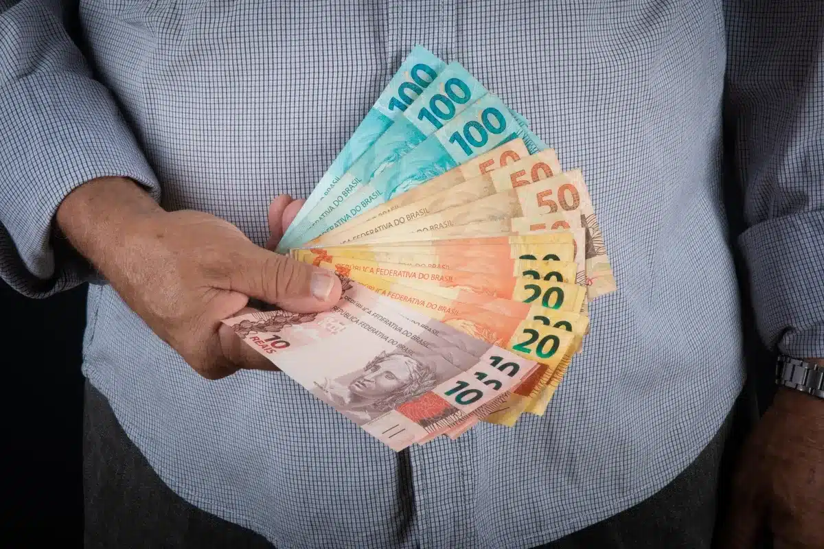 Pessoa segurando várias cédulas de reais, representando o 13º salário do INSS e o planejamento financeiro