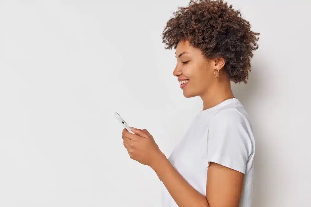 Mulher sorridente usando um smartphone, representando o processo de aposta na Dupla de Páscoa 2026
