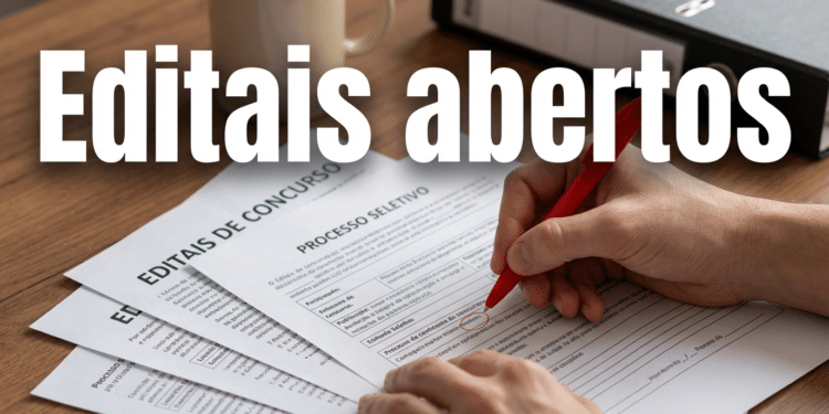 Mão segurando caneta vermelha sobre documentos de editais de concurso e processo seletivo em mesa de madeira