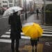 Adulto e criança com guarda-chuvas aguardam para atravessar uma rua sob forte chuva em ambiente urbano, representando os efeitos climáticos do El Niño.